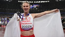 Maria Żodzik (fot. PAP/Adam Warżawa) Maria Żodzik z dumą prezentuje srebrny medal zdobyty podczas zawodów, stojąc na stadionie z rozpostartą biało-czerwoną flagą Polski. Na jej twarzy widać radość i wzruszenie, a medal zawieszony na szyi jest symbolem wielkiego sportowego sukcesu