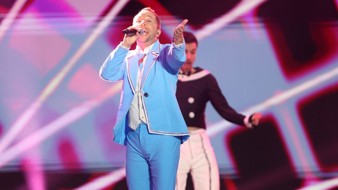 DJ BoBo w błękitnym garniturze. W jednej ręce trzyma mikrofon, drugą kieruje w stronę publiczności.