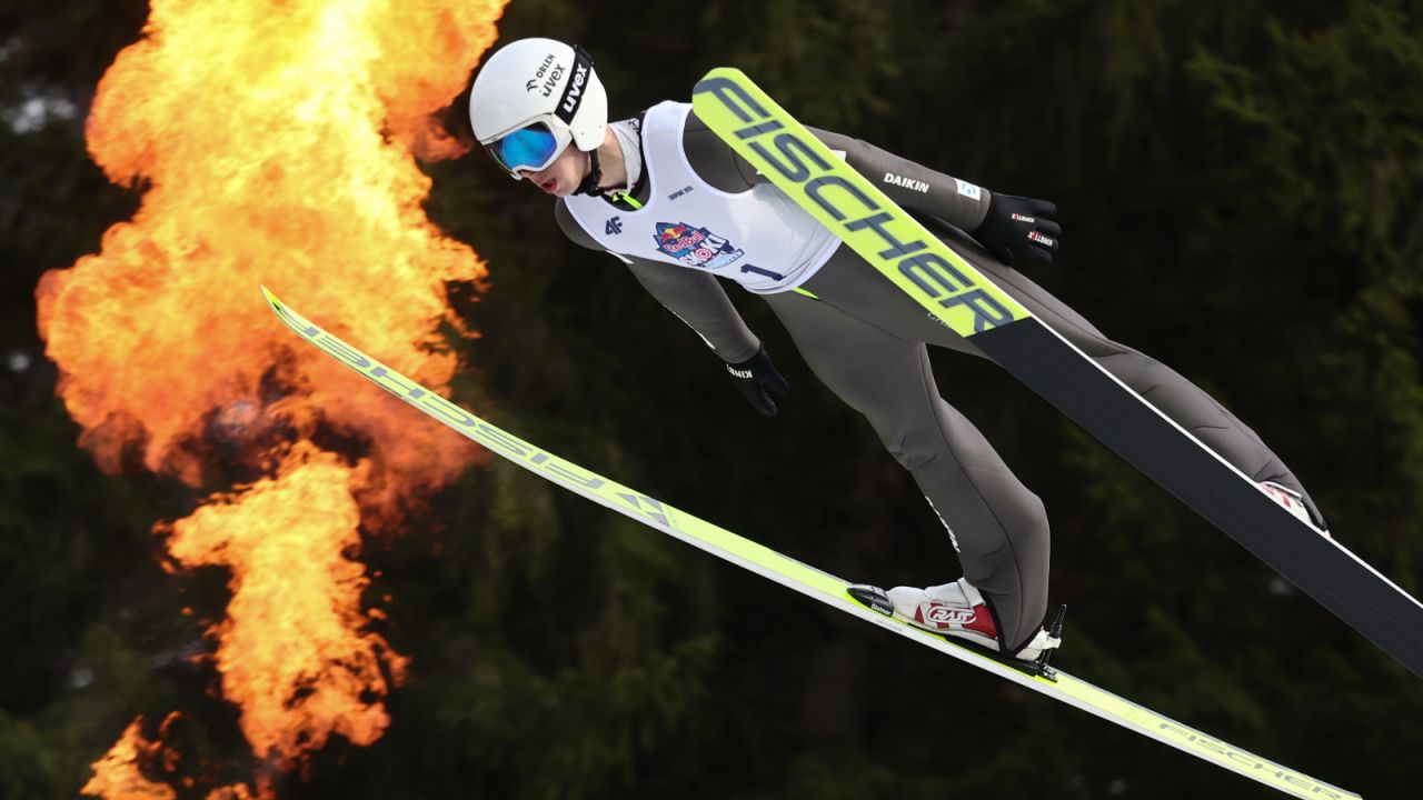 Kacper Tomasiak unosi się w powietrzu podczas efektownego skoku. Ubrany w biały kask Uvex i numer startowy z logo Red Bulla, Tomasiak symbolicznie wkracza na wielką scenę — Puchar Świata. Jego narty Fischer przecinają powietrze, a dynamiczne tło podkreśla intensywność emocji towarzyszących debiutowi. To nie tylko sportowy moment, ale wizualna zapowiedź nowego rozdziału w karierze młodego zawodnika, który według Sławomira Hankusa ma wystartować w pierwszych dwunastu konkursach sezonu (fot. Getty Images)