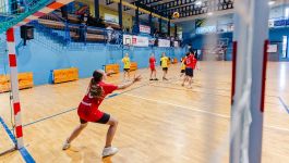 Na zdjęciu młodzi zawodnicy rywalizują w emocjonującym meczu w hali sportowej. Bramkarz w czerwonej koszulce stara się zatrzymać rzut przeciwnika, który właśnie wyskoczył w powietrze. Obserwujący akcję zawodnicy w żółtych strojach dodają napięcia tej dynamicznej scenie. Już za miesiąc wielki finał ogólnopolskiego turnieju Z Orlika na Stadion — emocje gwarantowane! (fot. materiały prasowe)