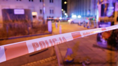 Fragment miasta w nocy i widok na oświetlone budynki i ulice. Na pierwszym planie biało-pomarańczowa taśma z napisem „Policja”.