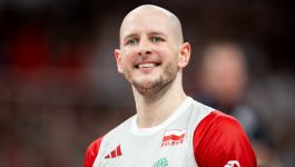 Bartosz Kurek (fot. Getty Images) Na zdjęciu widać uśmiechniętego Bartosza Kurka w barwach reprezentacji Polski. Zawodnik ma na sobie biało-czerwoną koszulkę z godłem Polski oraz logotypami sponsorów. W tle widać rozmazaną halę sportową wypełnioną kibicami, co sugeruje, że fotografia została wykonana podczas meczu lub turnieju reprezentacyjnego.